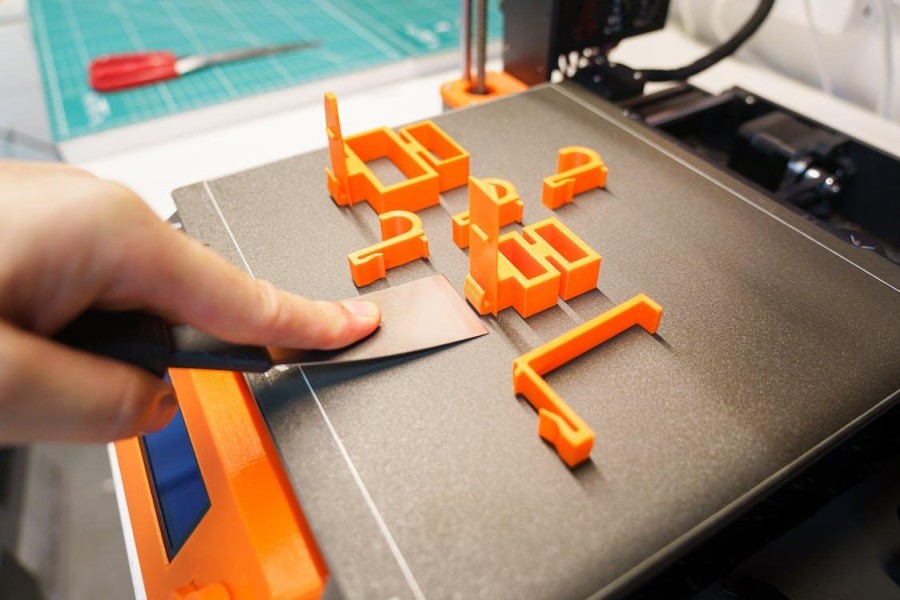 orangene Teilchen auf 3D-Drucker Platte und Hand mit Schaber